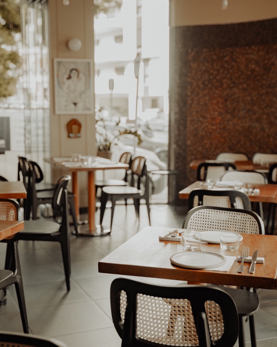 An empty dining room set for service, rattan chairs and laid tables by the window