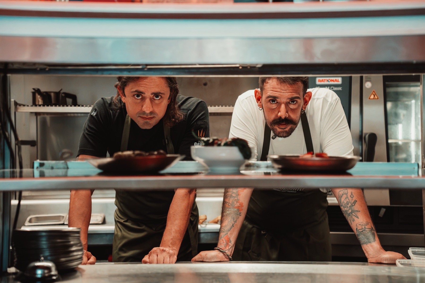 Two chefs leaning over the pass in a restaurant kitchen
