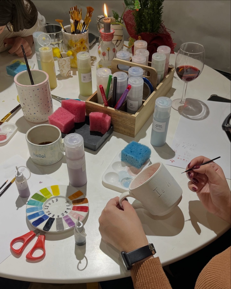 Hands painting a mug by candlelight at a Yiart class, a glass of red wine on the table